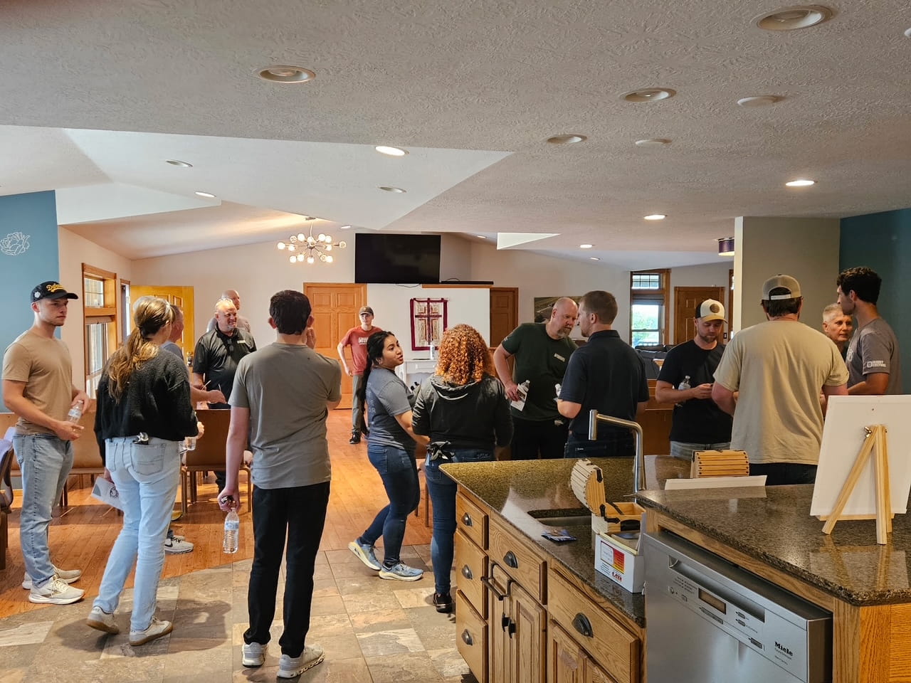 A group of people talking around the kitchen island and in the living area beyond it