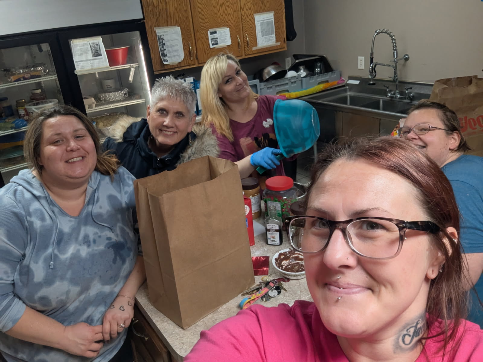 Five women packing a grocery bag with food in a kitchen