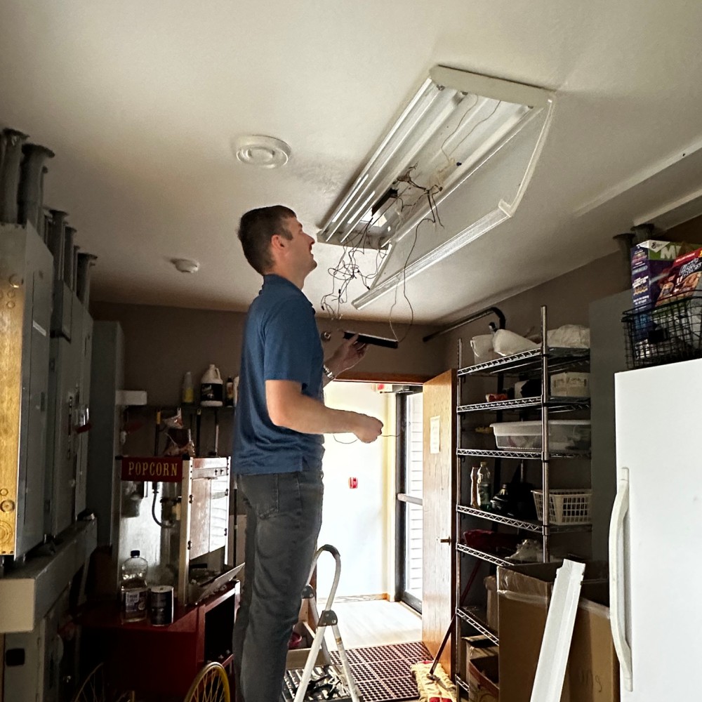 A person working on an open ceiling light with wires hanging down in a storage room
