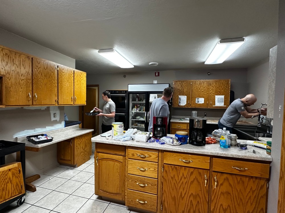 Three people in a kitchen, one washing dishes and another holding a pan