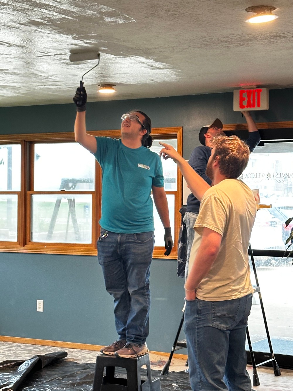 Three people painting a room, one rolling paint onto the ceiling from a step stool