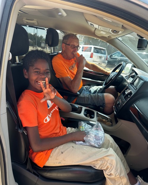 A child in the passenger seat smiles and holds up a peace sign while an adult sits in the driver's seat